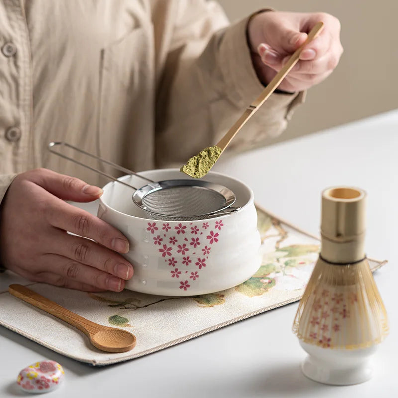 Japanese matcha set with white ceramic tea bowl and pink cherry blossom design, bamboo whisk, sifter, and tea scoop for traditional tea ceremony