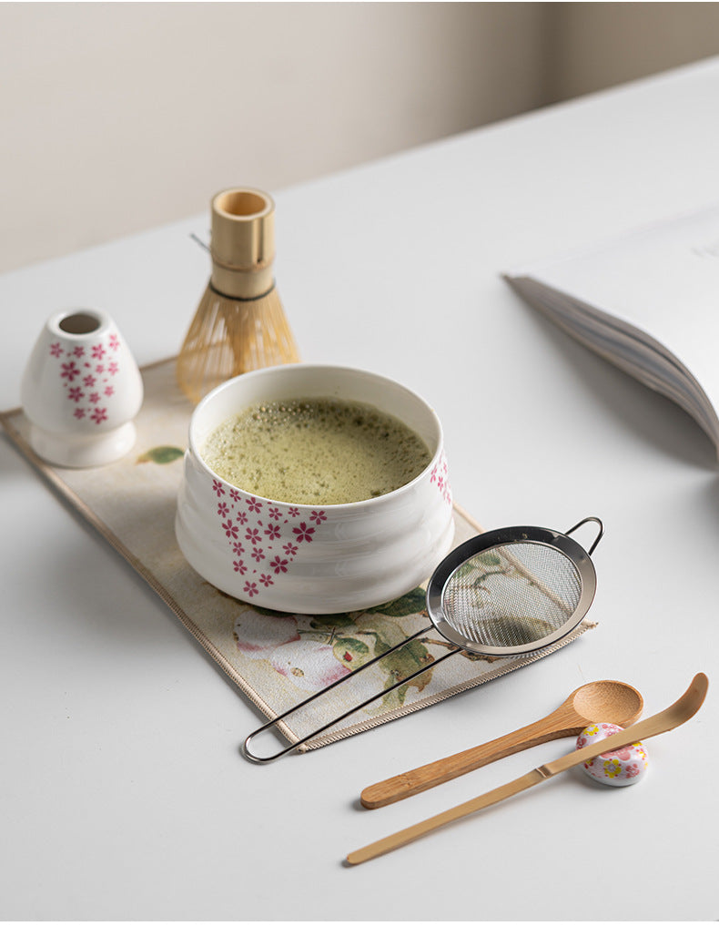 Japanese matcha set with white ceramic tea bowl and pink cherry blossom design, bamboo whisk, sifter, and tea scoop for traditional tea ceremony