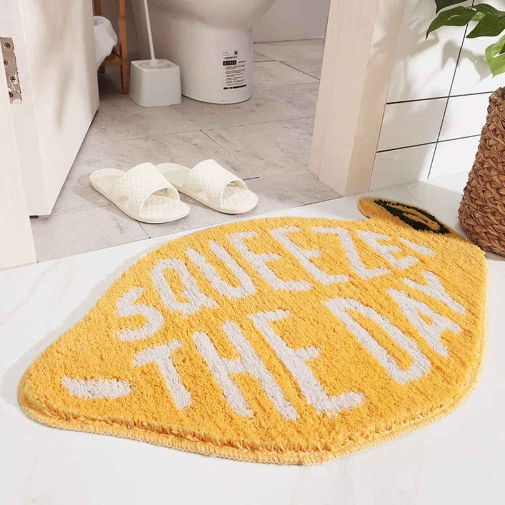 Yellow lemon-shaped bathroom rug with white text ‘Squeeze the Day’, soft absorbent bath mat