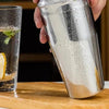 Premium stainless steel cocktail shaker set with mixing spoon, citrus slices, and bar tools – professional bartender kit for home and party drinks