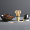 Minimalist Japanese matcha set with black ceramic tea bowl, bamboo whisk, whisk holder, and bamboo tea scoop for authentic tea ceremony