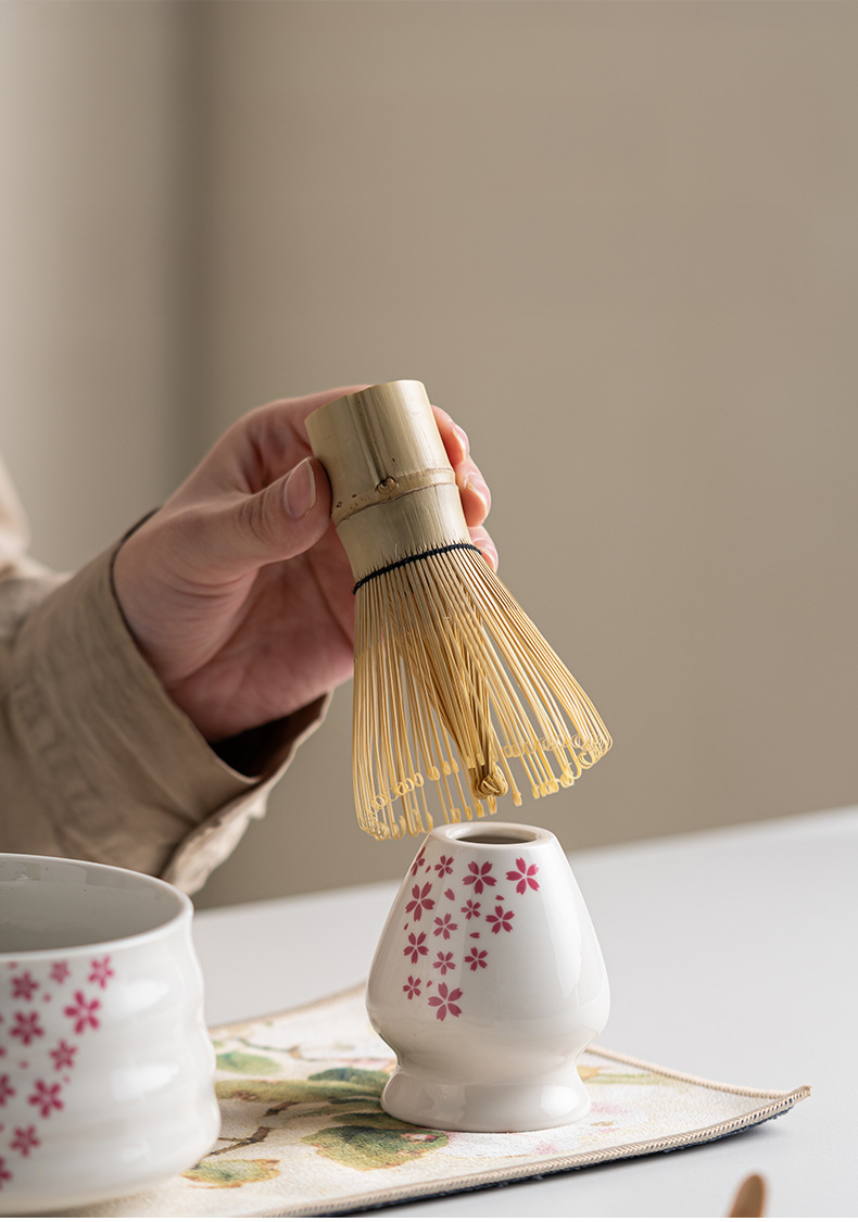 Japanese matcha set with white ceramic tea bowl and pink cherry blossom design, bamboo whisk, sifter, and tea scoop for traditional tea ceremony